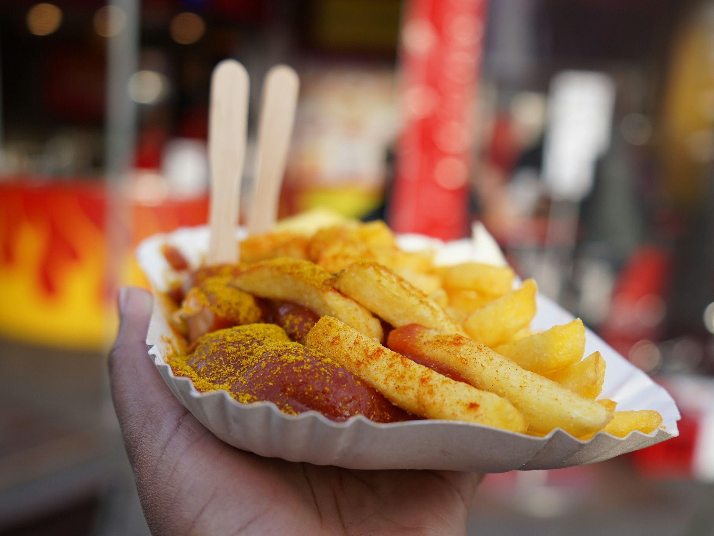 Hand hält Schale mit Currywurst und Pommes